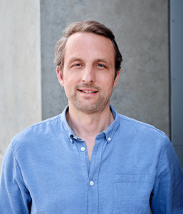 headshot of co-founder Jerome he is wearing a blue shirt with a grey background