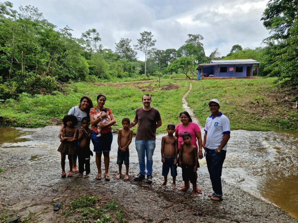 Image of locals and children standing in front of a field in a rainforest
